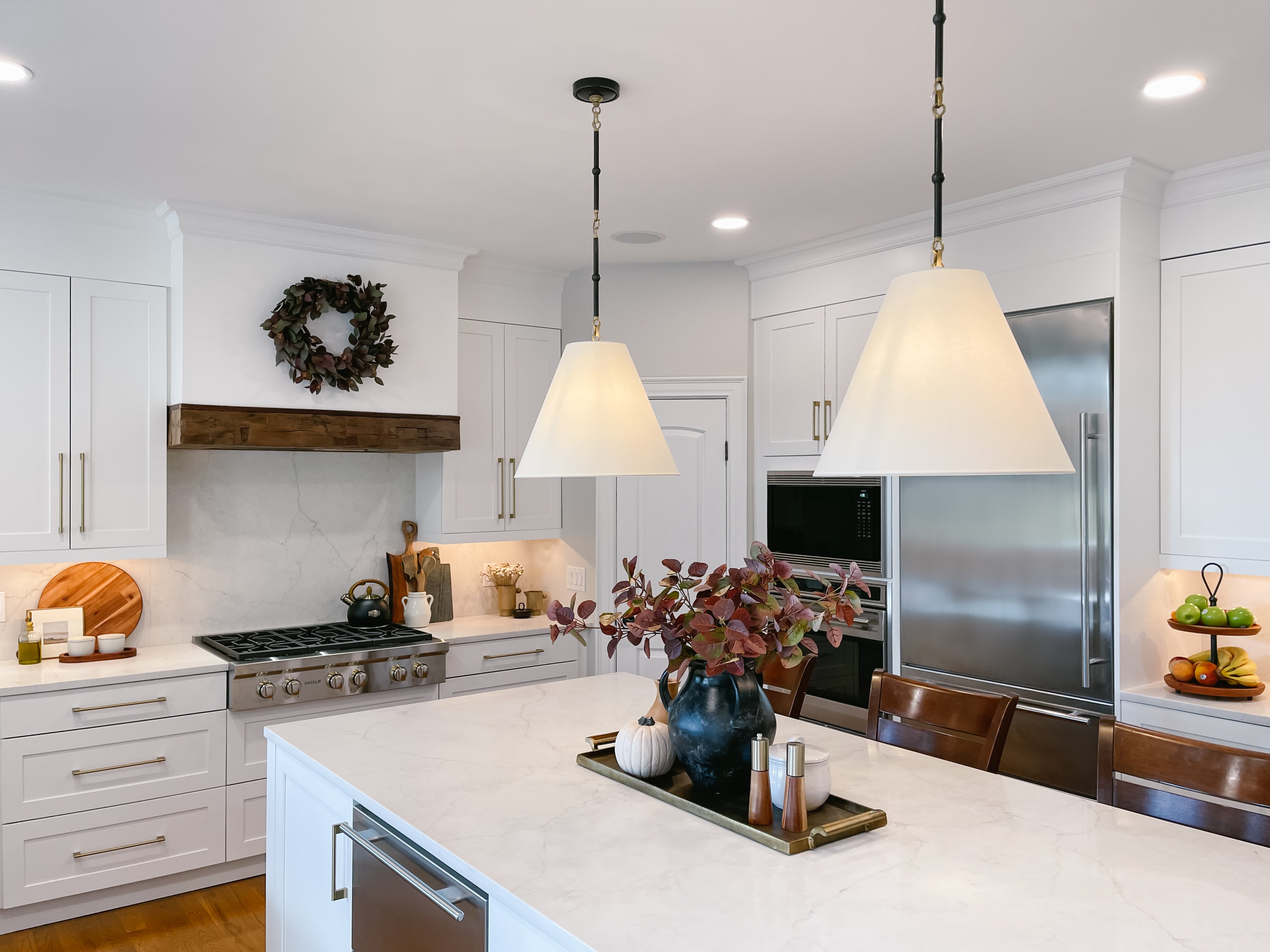 Farmhouse, mid-century style kitchen with white cabinets, subtly marbled quartz countertops and backsplash, a large island, custom hood, and custom light fixtures. 1/2