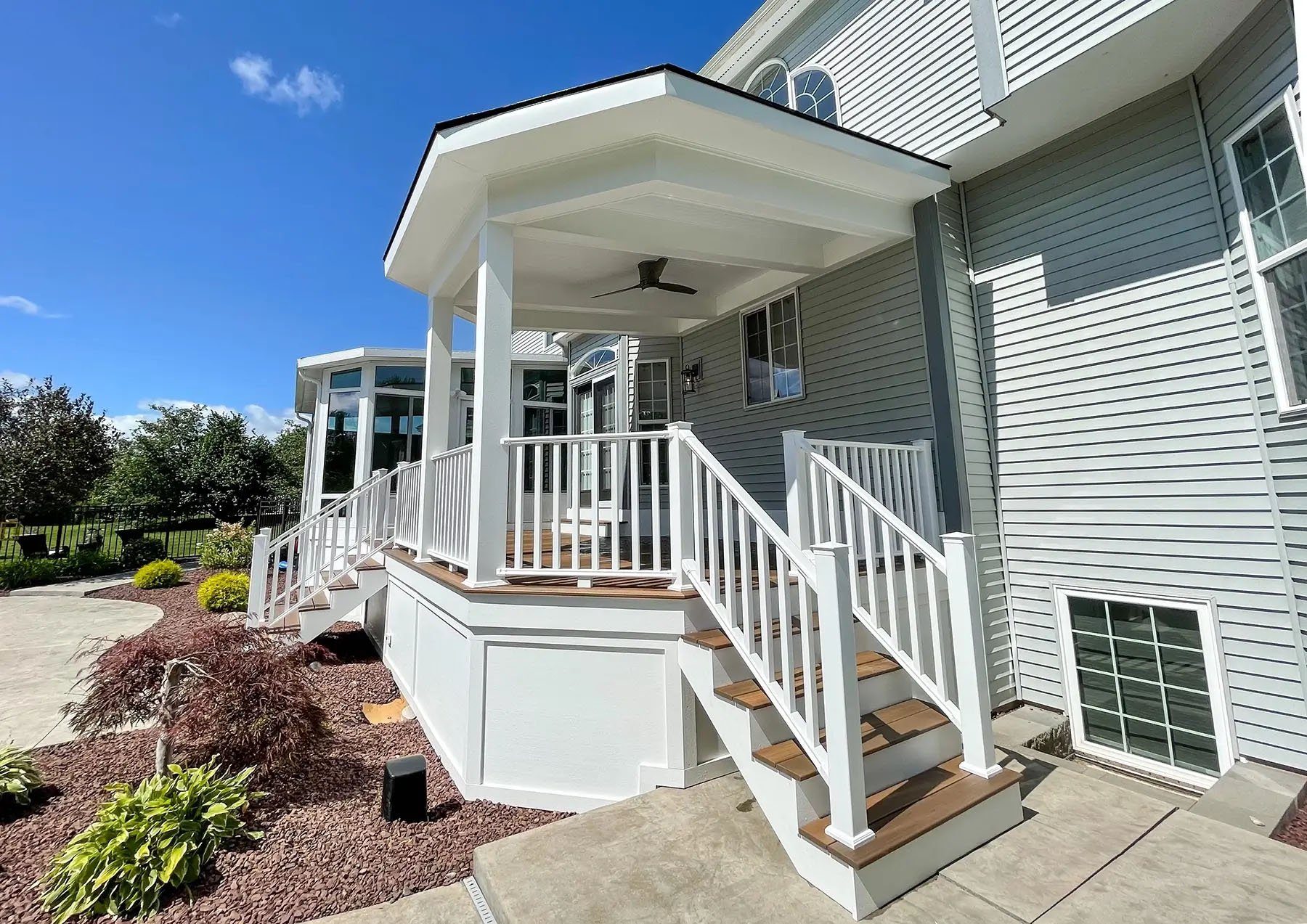Large outdoor composite deck with two sets of stairs, beam accents, and outdoor fan.