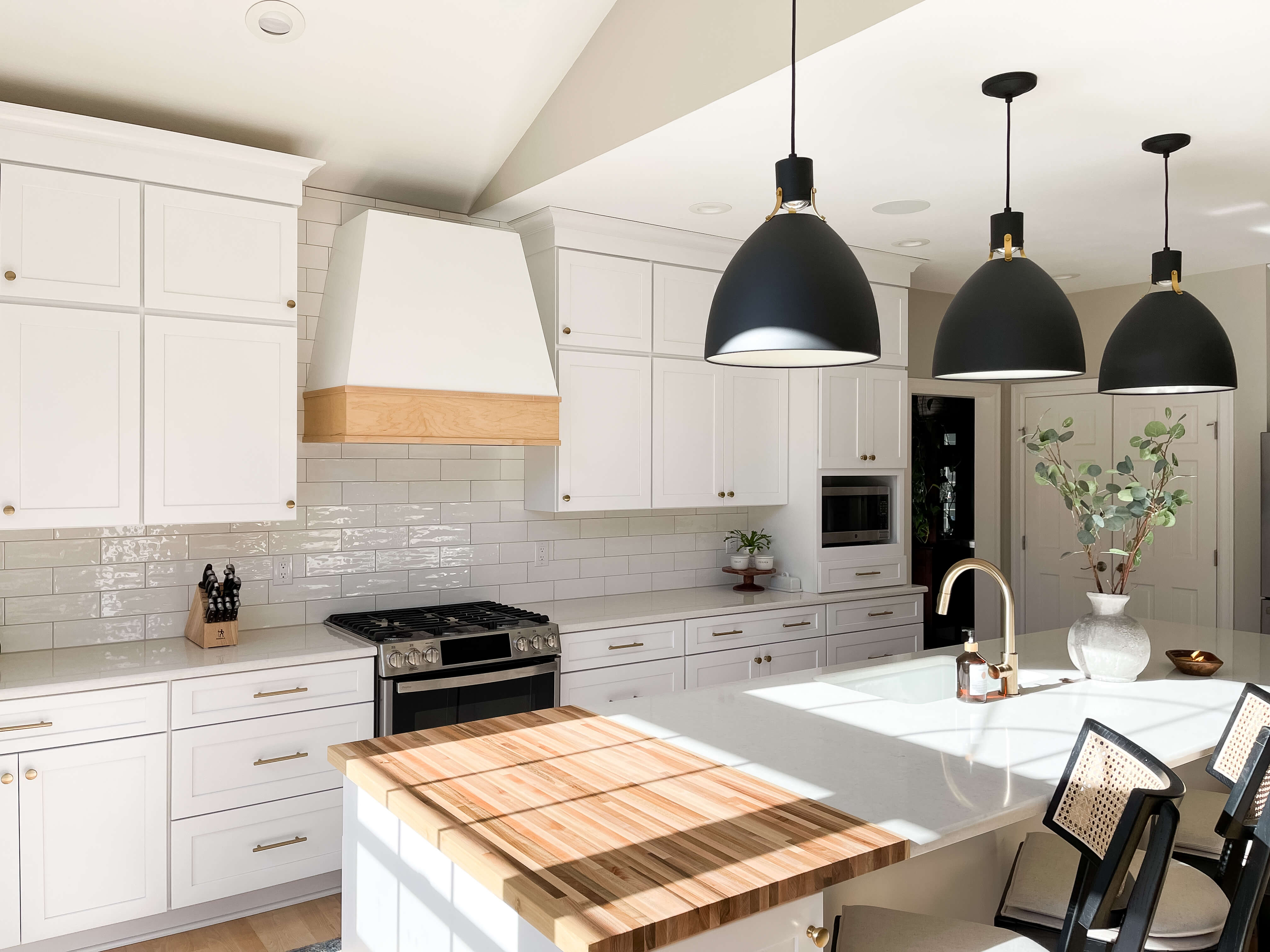 Kitchen featuring white quartz countertops, custom cabinetry, a butcher block island detail, and layered lighting throughout the space.