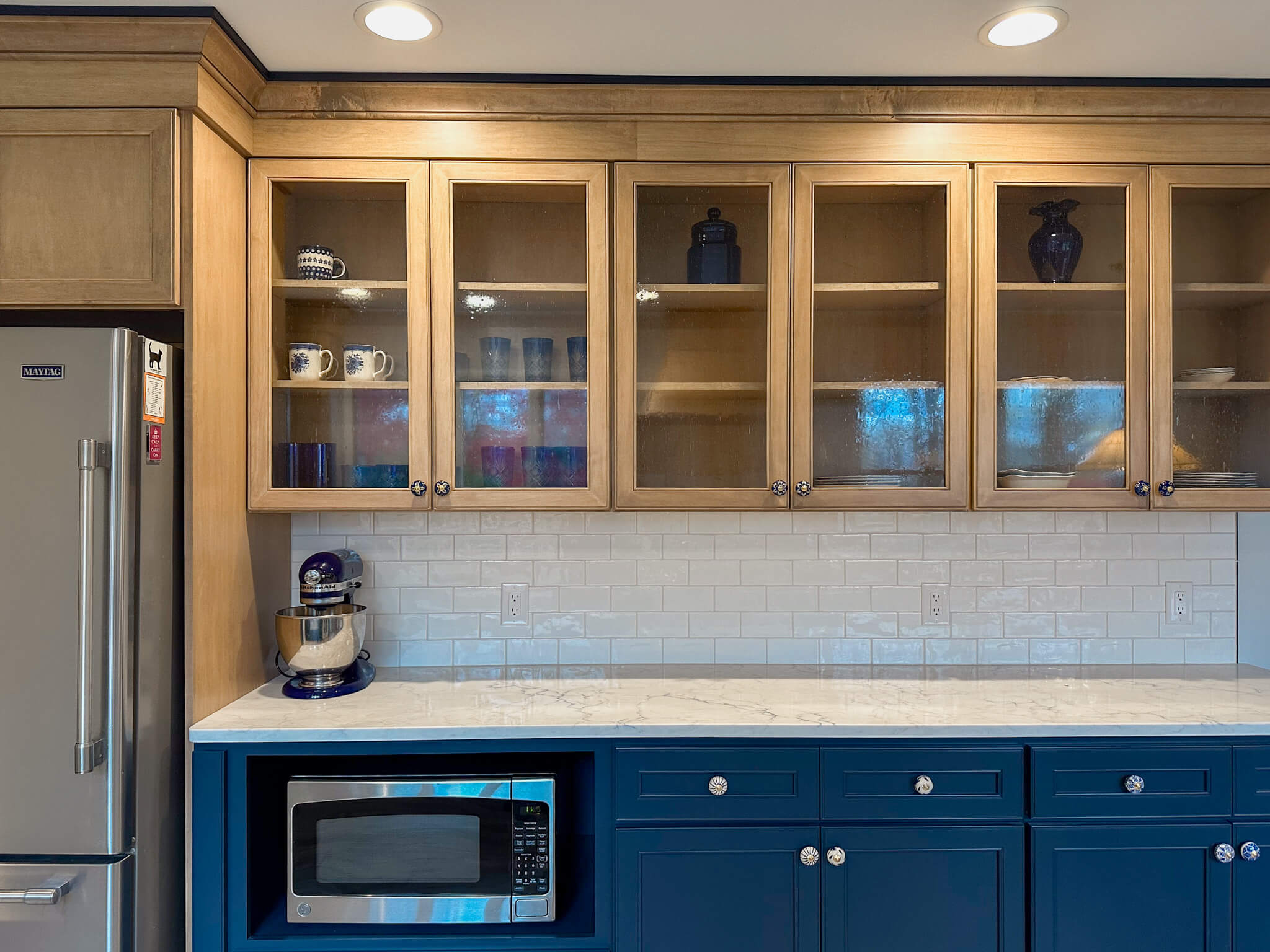 Kitchen featuring a quartz countertop, wood upper cabinets with glass-fronts, blue base cabinets, and a functional, well-organized layout.