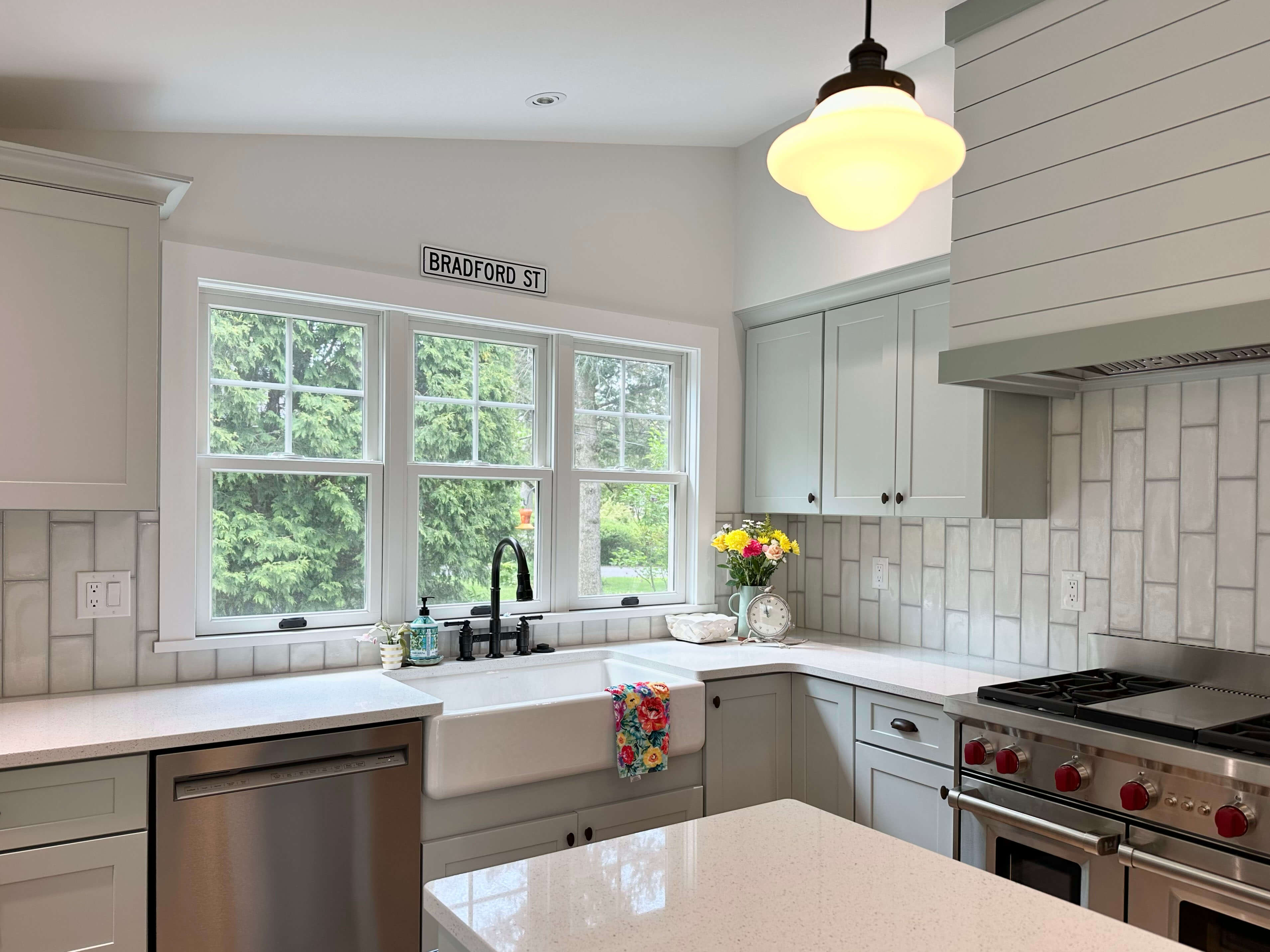 Kitchen featuring quartz countertops, farmhouse sink, light green cabinets, subway-style backsplash, and a clean, functional layout.