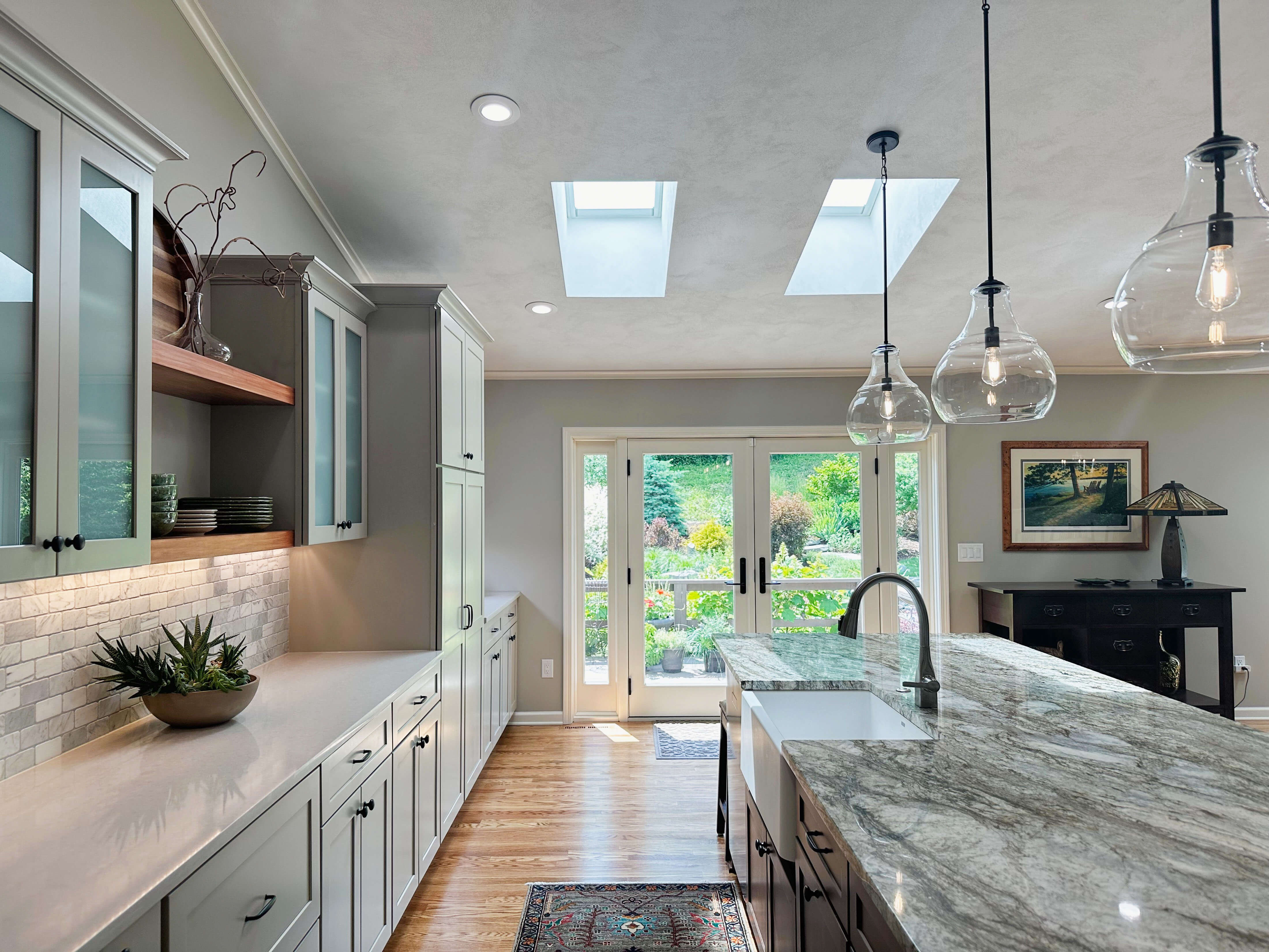 Kitchen featuring quartz countertops, a natural stone island with integrated sink, skylights, and layered lighting throughout the space.