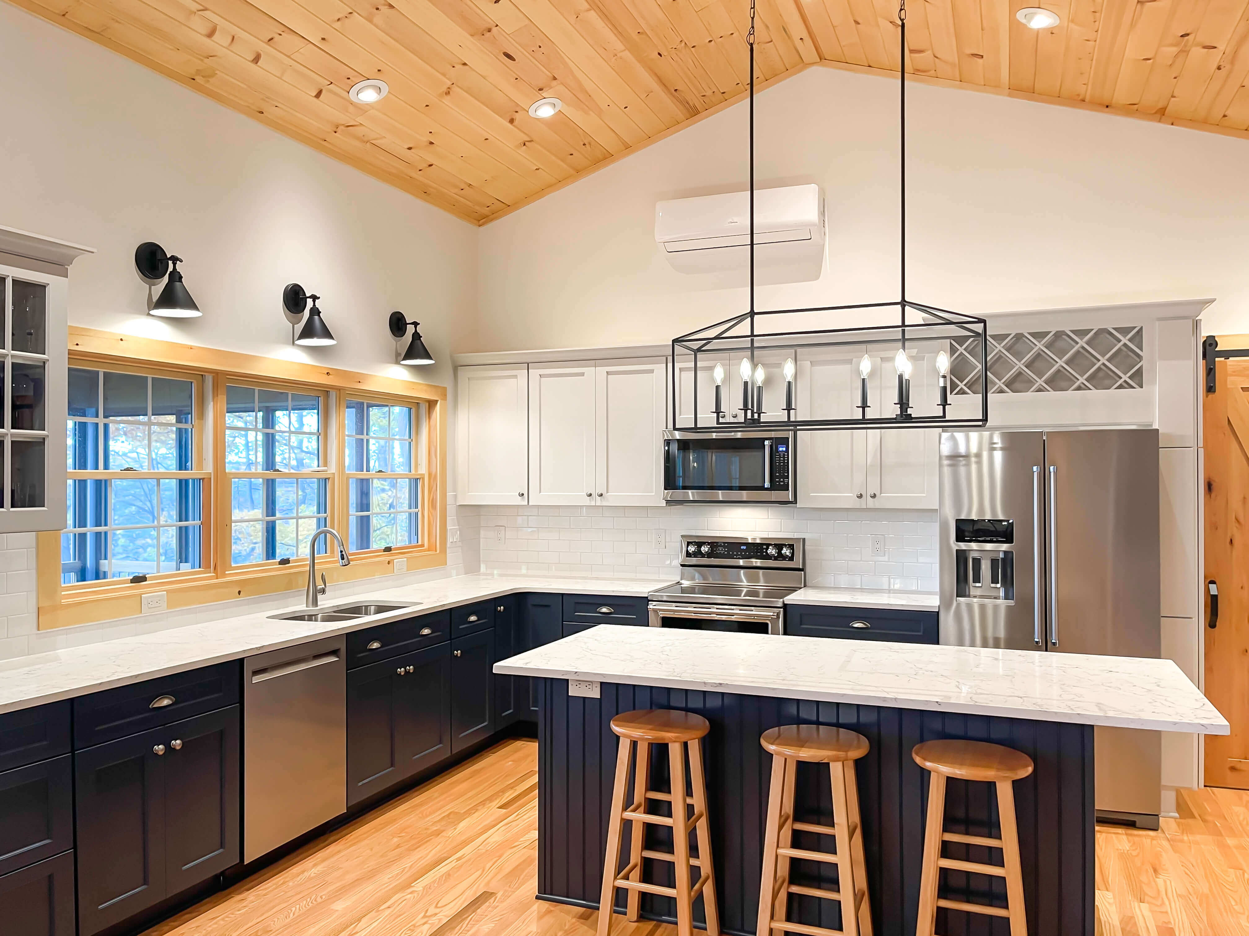 Bright kitchen with vaulted wood ceiling, industrial sconces, recessed LED lights, and a large black industrial chandelier providing ambient and task lighting.