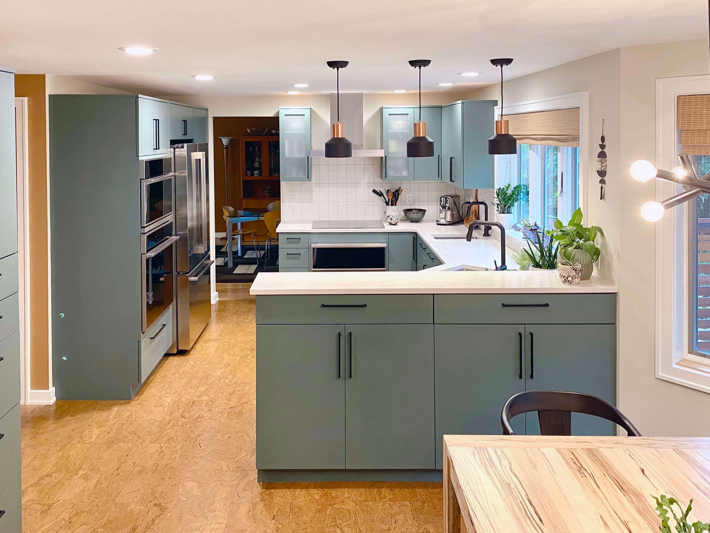 Sleek and ontemporary kitchen design with clean lines, green cabinets, vertical subway tile backsplash, mixed lighting including pendant task lights, recessed ambient lights, and natural window lighting for a bright, inviting space.