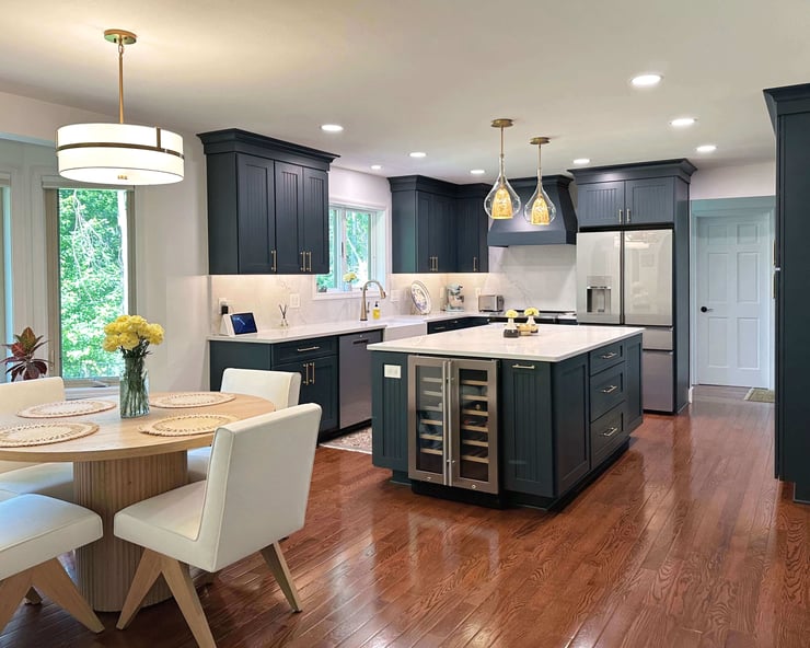 Transitional navy blue kitchen with layered lighting including recessed ceiling lights, glass pendant lights over the island, and a drum pendant above the dining nook.
