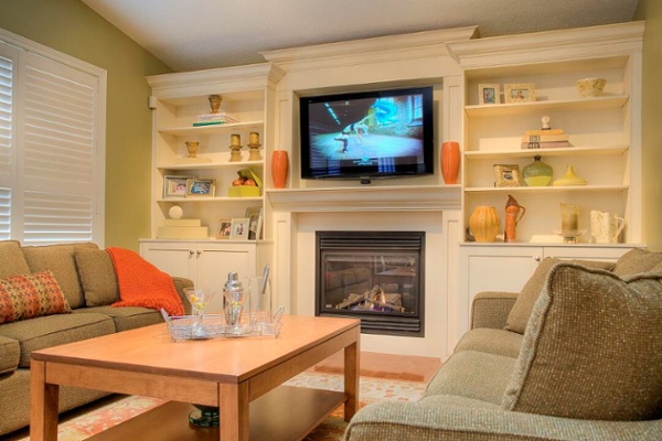 A built-in entertainment center encases a gas fireplace and a flat screen television. Cabinet doors hide video components. Open shelves provide a place for photos, books and collectibles. Crown molding adds architectural detail to the room. Photo courtesy of Elmwood Fine Custom Cabinetry.