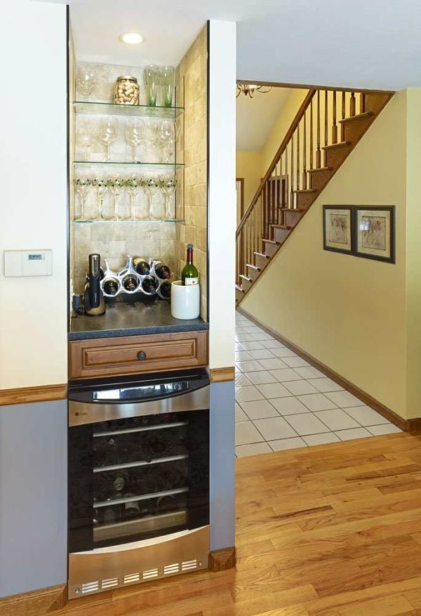 The small nook in this kitchen was remodeled into a bar area complete with glass shelving and a wine refrigerator lit by a small recessed light.