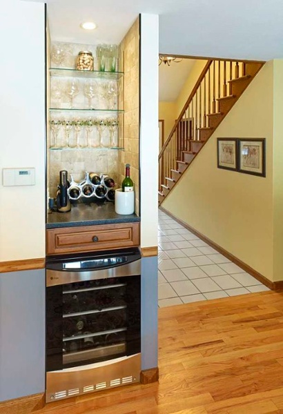 The small nook in this kitchen was remodeled into a bar area complete with glass shelving and a wine refrigerator lit by a small recessed light.